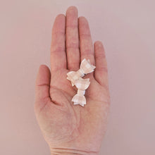 A pair of small brown and white gingham bow hair clips held in a hand against a pink background