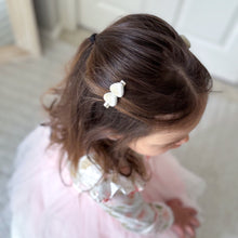 Brunette preschool-aged child with a silver coloured 4cm alligator hair clip embellished with 2 soft white ribbed velvety heart embellishments wearing a pink outfit indoors