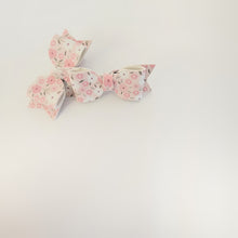 Pair of faux leather hair bow clips with a pink and white floral pattern, arranged on a plain white background.