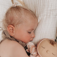 Toddler wearing a tiny brown and white  gingham bow holding a plush toy with a neutral background