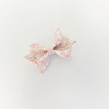 A faux leather hair bow with a delicate pink and white floral pattern, photographed on a clean white background.