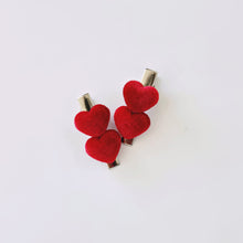 A pair of 4cm silver covered hair clips with heart-shaped embellishments in a red, velvety ribbed fabric.