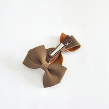A brown, faux suede hair bow accessory on a silver coloured metal alligator clip, wrapped in brown grosgrain ribbon, photographed on a clean white background.