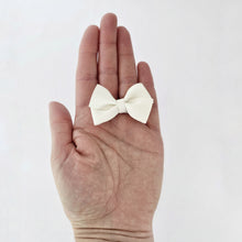 Small white hair bow clip on a person's palm against a light background